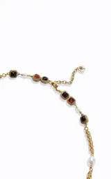 Collar largo de estilo sofisticado con cadena de metal en acabado dorado. Presenta un diseño intercalado con perlas sintéticas y detalles geométricos cuadrados con piedras en tonos rojizos y marrones.