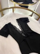 Body entallado de lycra color negro, con escote pronunciado decorado con encaje y microtul. Presenta mangas cortas de encaje y un collarín regulable desmontable integrado al diseño.