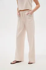 Pantalón ancho de viscosa color beige claro, de tiro alto con cintura elastizada y cordón ajustable. Presenta bolsillos laterales decorados con detalles bordados geométricos.