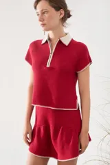 Top tejido de punto color rojo con cuello polo blanco, medio cierre frontal y detalles de costuras visibles en contraste en los bordes de las mangas y el ruedo.