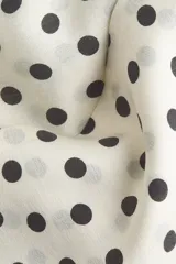 Blusa de gasa color beige con estampado de lunares negros, cuello alto con moña integrada y mangas largas abullonadas con puños ajustados.