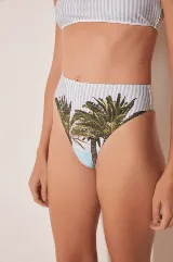 Conjunto de bikini con corpiño de tirantes con estampado a rayas verticales en blanco y celeste, y bombacha de tiro alto con estampado de palmeras y cielo celeste.