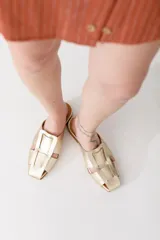 Zueco de cuero color marrón, estilo mule, con puntera cuadrada y tira ancha adornada con flecos. Suela plana.