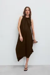 Vestido midi de color marrón con acabado satinado, cuello redondo con detalle fruncido y diseño sin mangas. Presenta un corte fluido con bajo asimétrico y bolsillos laterales ocultos.
