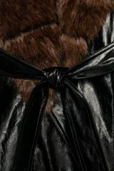 Trench corto Zara de efecto piel color negro, con cuello de solapa y aplicación de pelo sintético a contraste en color marrón. Cuenta con manga larga con trabillas en los puños, bolsillos delanteros y cinturón ajustable del mismo tejido.