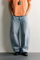 Jeans de denim de algodón color gris con efecto lavado, de corte relaxed barrel fit y tiro medio. Presenta diseño amplio con pinzas en las rodillas y costuras curvas, cierre frontal con botones y cinco bolsillos tradicionales.