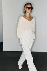 Jersey de punto de color blanco crudo, con escote en V y mangas largas con sisas amplias y puños elásticos acanalados.