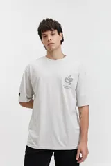 Remera oversize de algodón con efecto acid wash, color blanco hueso. Estampado grande en la espalda con un diseño circular que incluye una serpiente enroscada, texto "MISTRAL REG", "LOS ANGELES", "CALIFORNIA", "VINTAGE DENIM", "REGISTERED" y "TM 76".