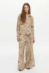 Camisa beige de manga larga, con cuello camisero, cierre frontal con botones y un estampado detallado de motivos botánicos e insectos en tonos oscuros.