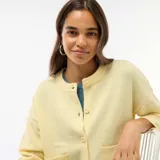 Cardigan de punto color amarillo suave, con cuello redondo, cierre frontal de botones y dos bolsillos de parche delanteros. Presenta mangas largas con puños acanalados y un corte recto.