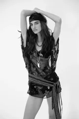Vestido corto de tul negro con transparencias, bordado con lentejuelas y motivos florales. Presenta mangas cortas tipo kimono, escote en V y un cinturón de tela con flecos y detalles brillantes. Incluye un viso interior a tono.