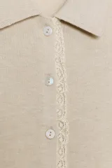 Chaqueta de manga corta y punto en color beige, con cuello polo y cierre frontal de botones. Presenta detalles de puntilla a contraste en la botonera y los puños.