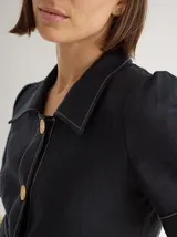 Chaqueta de lino color negro con costuras a contratono, mangas cortas con dobladillo y detalle de franja texturizada en la cintura. Presenta cuello camisero y etiqueta de cuero en la espalda.