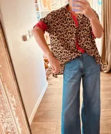 Camisa de manga corta con estampado animal print y detalles en rojo intenso en cuello y puños. Corte holgado y cierre frontal con botones.