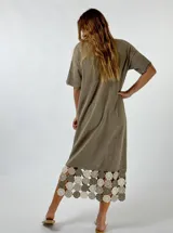 Vestido midi de tejido ligero color beige, con cuello en V, mangas cortas y ruedo decorado con aplicaciones de crochet en tonos tierra y rosado.