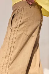 Pantalón de lino lavado color beige, de calce recto y diseño relajado. Presenta cintas de lino desflecadas aplicadas en los laterales con pespunte central, pretina con botón metálico, bolsillos delanteros y traseros.