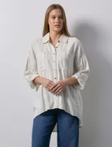 Camisa de lino a rayas verticales color crema, con cuello con solapa, abertura central con botones, bolsillos delanteros y mangas 3/4 regulables con presilla y botón.