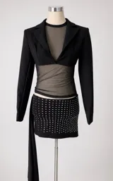 Conjunto de dos piezas compuesto por un blazer corto tipo torera de manga larga y una minifalda ajustada con detalle de strass brillante. La falda presenta un diseño drapeado y la chaqueta tiene un corte estructurado.