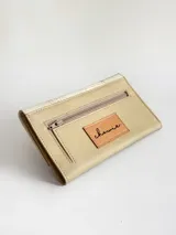 Billetera de cuero con diseño bicolor en tonos crema y beige. La solapa presenta una textura tipo reptil y detalles decorativos de cordones cruzados en los laterales. Cuenta con cierre mediante broche y monedero externo.