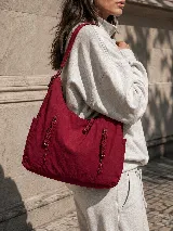 Cartera hobo gris de tela suave y liviana, con bolsillos frontales con cierre y tiradores trenzados, correa ajustable y compartimento principal con cierre.