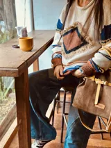 Bolso marrón de cuero gamuza con detalles de correa en cuero mostaza. Tiene una correa corta para llevar como bolso de mano y una correa larga extraíble y regulable. En el interior tiene bolsillo y llavero.