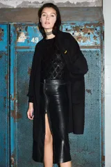 Falda midi de cuero ovino color negro, con diseño de tiro alto y cierre frontal completo con cremallera metálica. Presenta detalles de tachas decorativas a lo largo de la costura central y el borde del cierre.