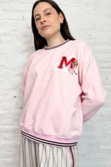 Buzo rosa de rústico con cuello, puños y ruedo acanalados con doble línea negra. Tiene un aplique con la letra M y una flor.