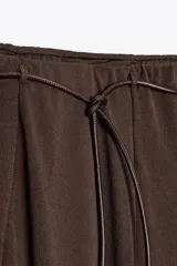 Falda larga de tiro medio, color beige claro, con caída amplia y cinturón fino negro anudado en la cintura.