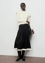 Falda midi de corte evasé en color negro, con diseño de tablas y detalle de vivo en color crema en el ruedo. Cuenta con cierre lateral.