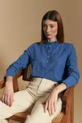 Blusa de algodón color azul con textura bordada, cuello con volado y cierre frontal con botones. Presenta mangas largas y un calce relajado.