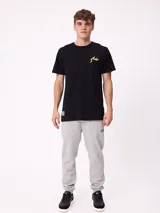 Remera de manga corta color crema con estampado gráfico en la espalda que representa un paisaje de montaña con un lago, árboles y una carpa, junto con el logo de la marca Rusty.