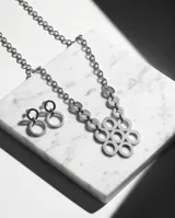 Set de joyería compuesto por un collar de cadena de eslabones con un dije central formado por círculos entrelazados y aros colgantes a juego con diseño circular.