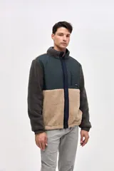 Campera de estilo outdoor con diseño de bloques de color, confeccionada en una combinación de sherpa y paneles de nylon capitoneado. Presenta cierre frontal con botones a presión, cuello alto, bolsillos laterales y un bolsillo en el pecho con cierre. Incluye puños elásticos y detalles bordados en la manga.