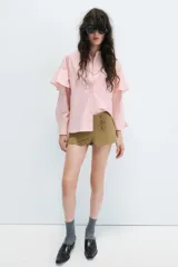 Camisa rosada de cuello solapa y manga larga, con detalle de volantes en las sisas y cierre frontal oculto con botones.