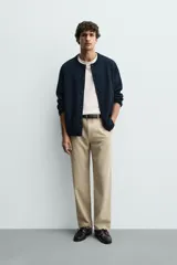 Pantalón de corte recto confeccionado en tejido elástico, con cintura elástica, pliegues frontales, bolsillos laterales y bolsillos traseros de vivo con botón.