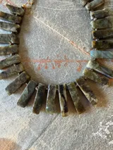 Collar corto elaborado con piedras naturales de labradorita en formato rectangular, unidas en secuencia con pequeños separadores metálicos dorados. Presenta cierre de mosquetón y cadena de extensión.