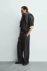 Pantalón de jeans de algodón ligero, color negro lavado, con corte balloon fit (holgado y ancho). Presenta pliegues frontales marcados en la cintura y cierre frontal de cremallera y botón.