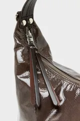 Bolso tipo hobo de diseño media luna, confeccionado en cuero caprino con acabado charol y textura grabada. Cuenta con cierre superior de cremallera, asa ajustable y el logo de la marca en la parte frontal.