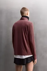 Sudadera técnica color vino tinto, de manga larga, con cuello subido y cierre frontal de cremallera. Presenta un bolsillo frontal con cierre de cremallera oculta en costura y detalle de logo estampado. El tejido tiene estructura waffle en el interior.
