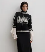 Campera tejida de algodón en color rojo, con cierre frontal completo, cuello alto y puños acanalados con detalles de rayas blancas. Presenta un diseño gráfico con texto blanco en el frente.