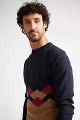 Sweater de punto con diseño color block, combinando azul marino en la parte superior, un patrón geométrico en tonos bordó y azul en el centro, y color camel en la parte inferior. Presenta cuello redondo y mangas largas.