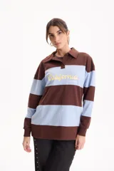 Buzo deportivo sin friza a rayas horizontales en tonos marrón y celeste, con cuello polo y cierre frontal parcial. Presenta estampa frontal con la inscripción "California" en color amarillo.