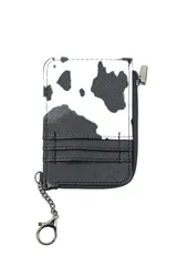 Billetera tarjetero con diseño estampado tipo animal print de vaca en blanco y negro, con sección inferior en cuerina negra que incluye ranuras para tarjetas. Posee cierre lateral, herrajes metálicos y una pequeña cadena con argolla para llavero.