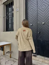 Sweater de plush color beige, de diseño holgado, manga larga y aberturas laterales en el dobladillo.