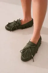 Mocasín de gamuza color marrón, con diseño de flecos decorativos en todo el contorno y la capellada. Presenta cordones decorativos con detalles metálicos dorados en las puntas.