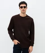 Buzo masculino de textura waffle, con cuello redondo y mangas largas. Confeccionado en una mezcla de algodón y poliéster, presenta un diseño cerrado y minimalista.