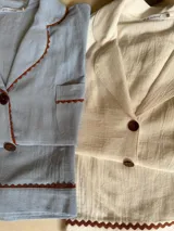 Pijama de algodón color celeste, compuesto por una camisa de manga corta con botones marrones y ribetes festoneados en color marrón, y un short con elástico en la cintura y ribetes festoneados en el ruedo.