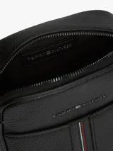Morral de cuero sintético con acabado granulado color negro, de Tommy Hilfiger. Cuenta con un compartimento principal con cierre de cremallera, bolsillo frontal decorado con una franja tricolor vertical, correa cruzada ajustable y el logo metálico de la marca en la parte superior.
