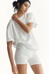 Remera de punto suave de algodón, de color blanco, con cuello redondo ribeteado y acanalado, corte holgado, hombros caídos y mangas cortas con doblez cosido.