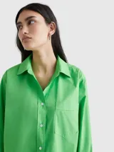 Camisa verde de popelín de algodón orgánico, corte oversize con hombros caídos, cuello inglés, bolsillo de parche en el pecho y logo bordado en la manga.